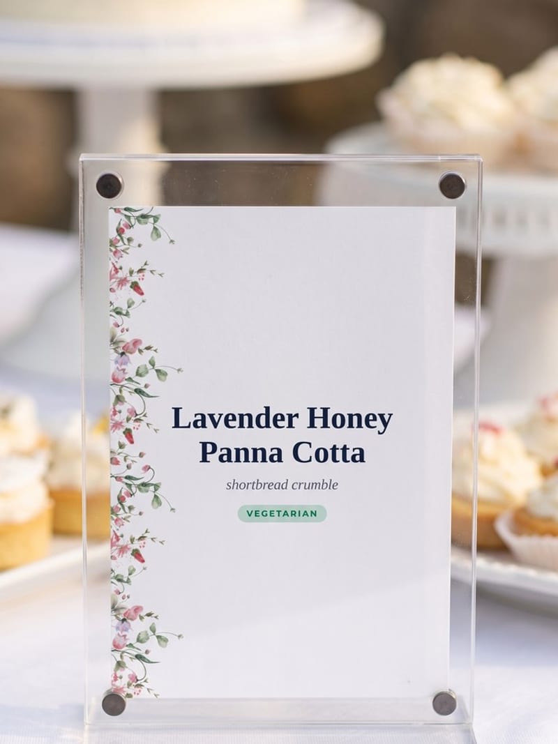 Wedding-Wild-Flower-themed 4 by 6 inch buffet label held between two clear acrylic panels by corner magnets, on a white dessert table with a cake stand and cupcakes behind it